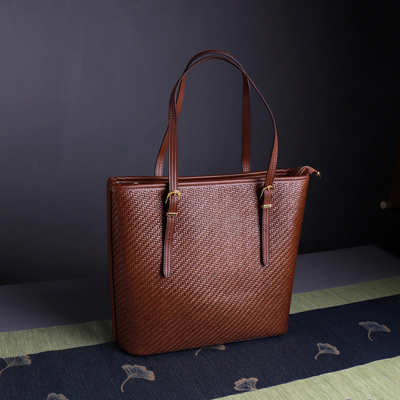 Brown woven straw large tote bag with leather handles, side details and top zipper